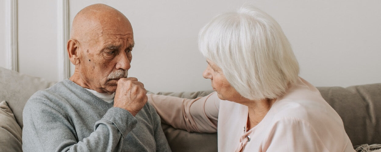 Elderly man coughing whilst being comforted by his wife